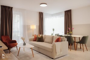 A modern living room with a sofa, armchair, coffee table, and dining area. - ZEN Garden Apartments (Cluj-Napoca)