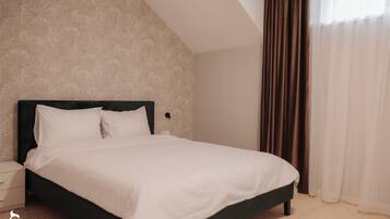 A neatly made bed in a room with a patterned wallpaper, a nightstand, and a window with curtains.