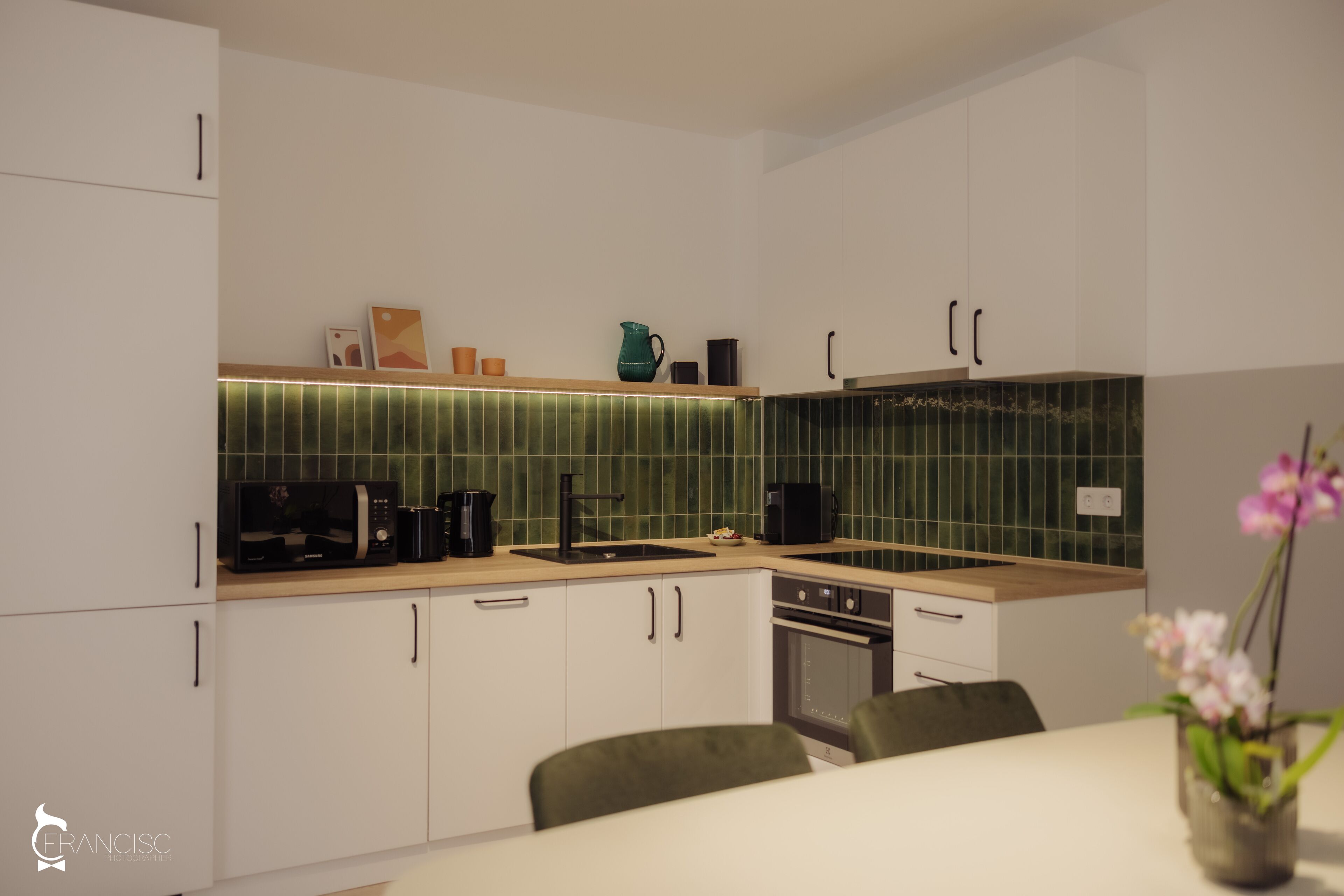 A modern kitchen with white cabinets, a green backsplash, and a dining area with a table and chairs.