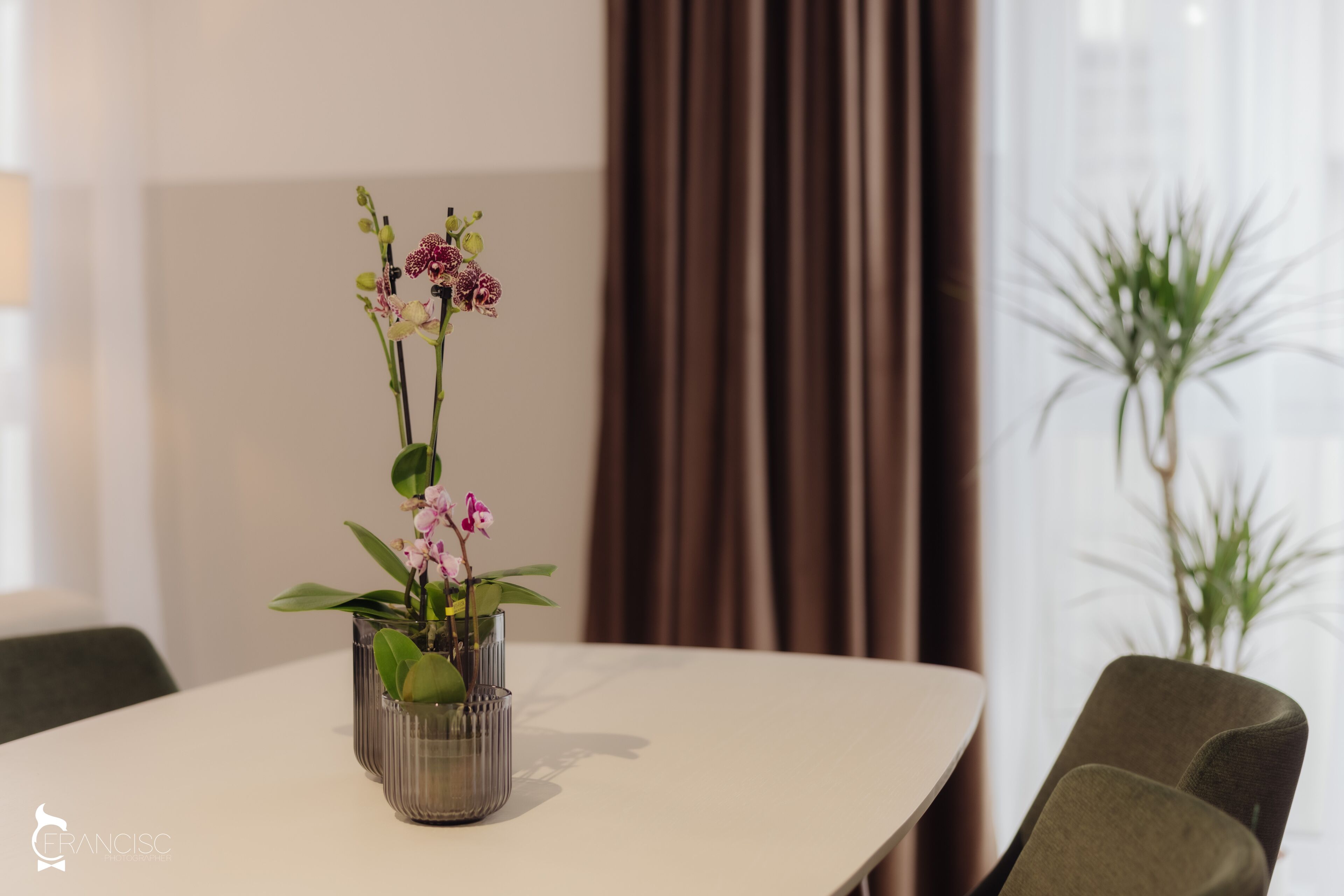 A dining table with a vase of orchids.