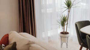 A modern living room with a sofa, a dining table, and two potted plants. - ZEN Garden Apartments (Cluj-Napoca)