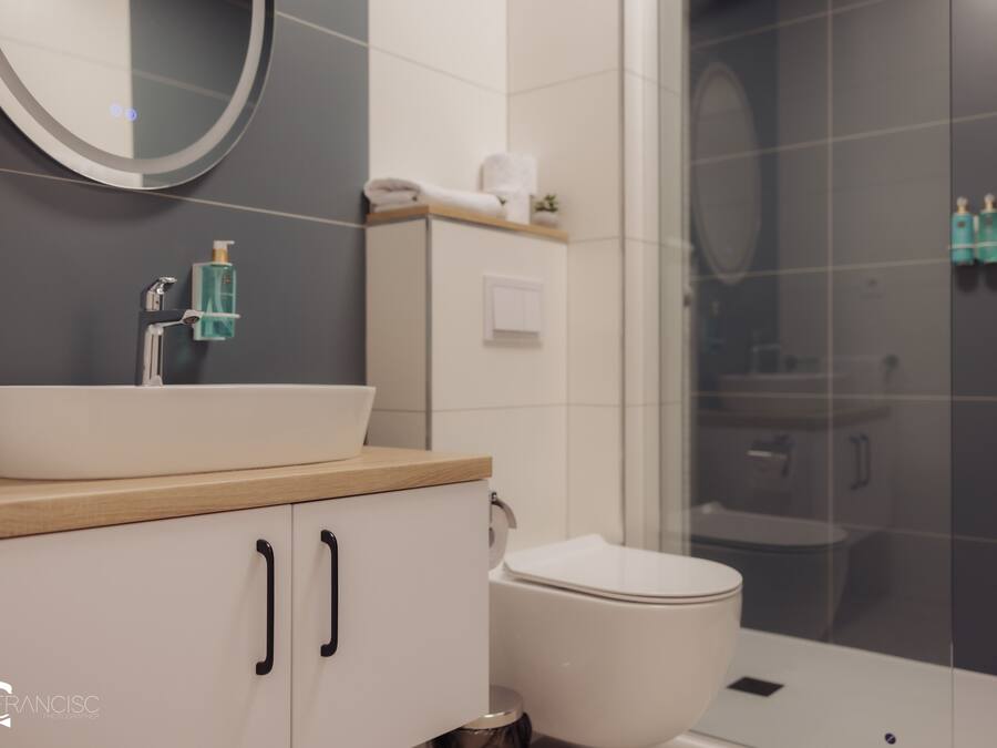 Une salle de bain moderne avec un lavabo blanc, un plan de toilette en bois et une cabine de douche en verre.