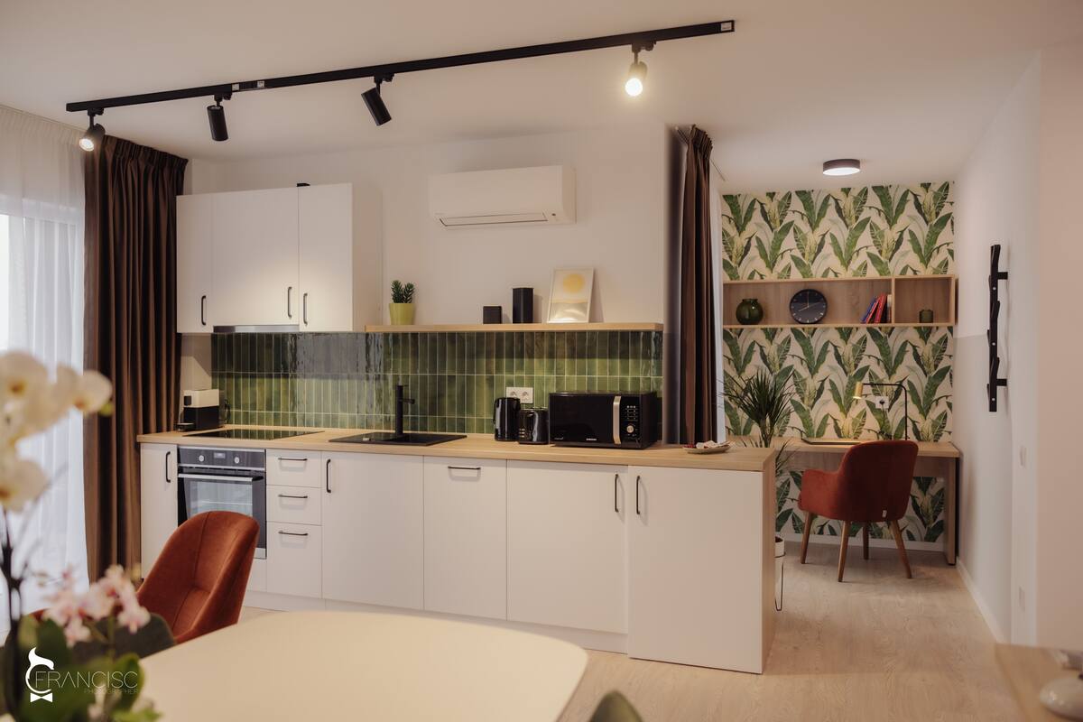 Eine moderne Küche mit weißen Schränken, einer Mikrowelle und einer Kaffeemaschine. Es gibt einen Essbereich mit Tisch und Stühlen.