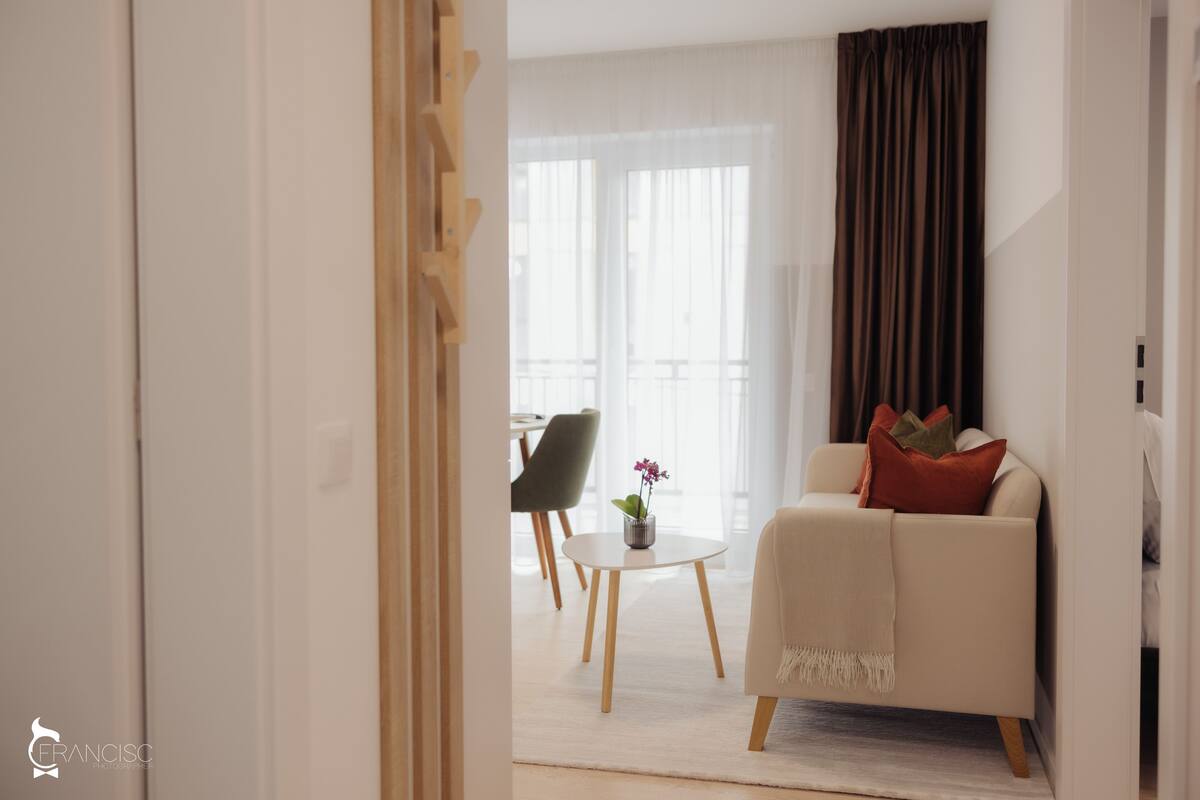 Ein modernes Wohnzimmer mit einer Couch, einem kleinen Tisch mit einer Vase und Blick auf einen Balkon.