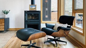 Un salon moderne doté d’un poêle à bois, d’un fauteuil en cuir confortable et d’une grande fenêtre donnant sur l’extérieur.