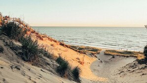 Une plage avec une promenade en bois menant à l’eau, des dunes de sable et un ciel dégagé.