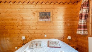 Ein Zimmer in einer Holzhütte mit einem Bett, zwei Nachttischlampen, einem Bild an der Wand und einem gemusterten Vorhang.