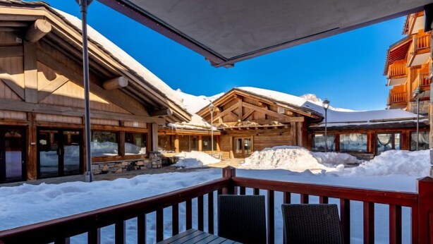 Eine Holzhütte mit überdachter Terrasse und Blick auf einen verschneiten Berg.