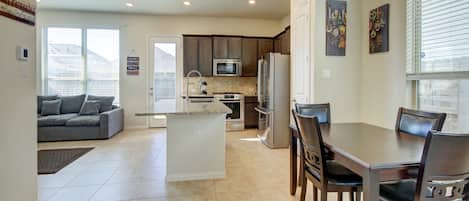 A spacious kitchen with a dining area, a gray sofa, and a large window.