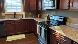 A kitchen with dark wooden cabinets, a stainless steel microwave, a black stove, granite countertops, and a window with blinds. - Five Stars Luxury Clean Home (Clarksville)