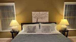 A bedroom with a bed, two bedside lamps, a wall art piece, and a window with blinds. - Five Stars Luxury Clean Home (Clarksville)