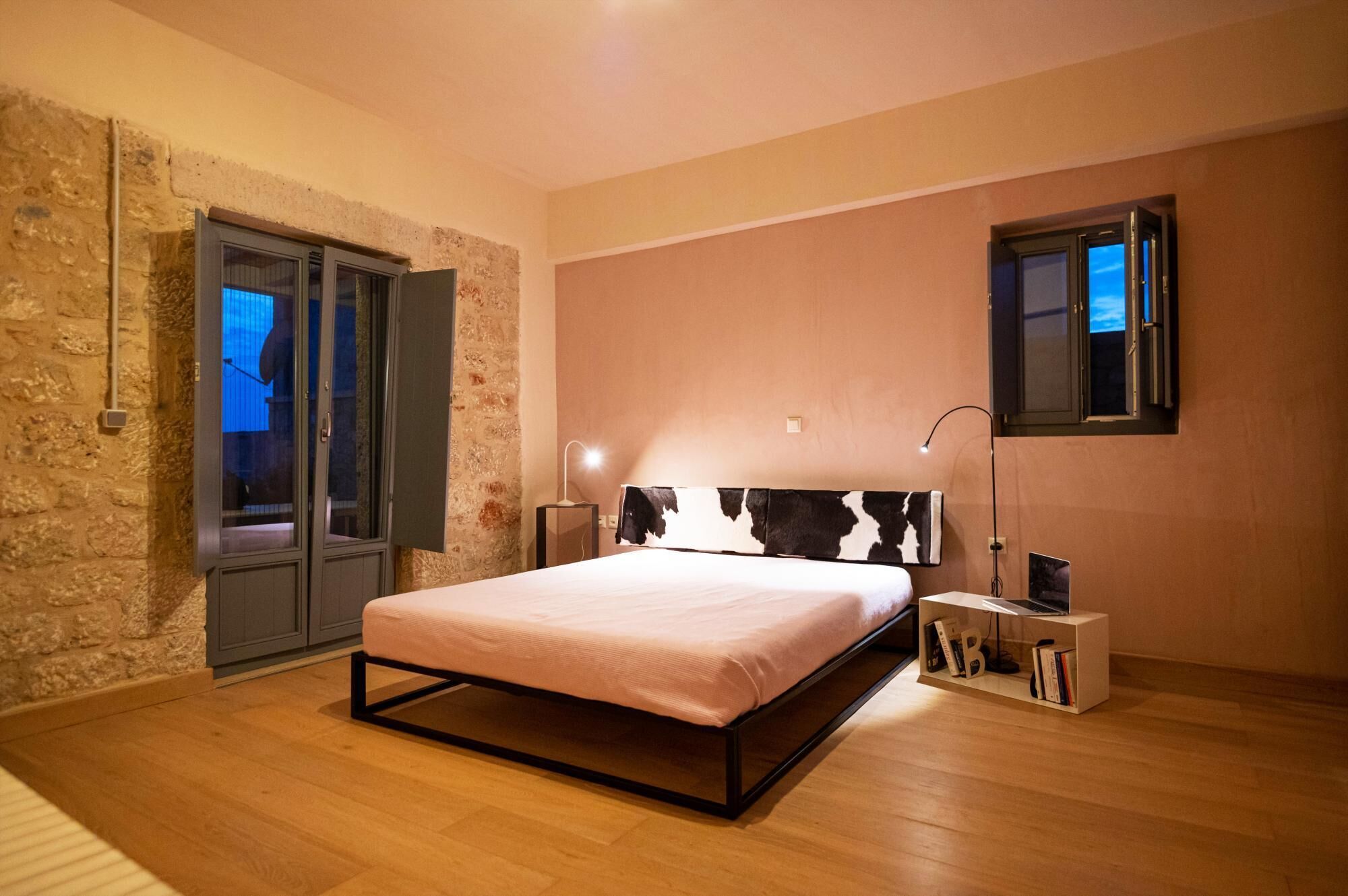 A bedroom with a bed, a nightstand, a bookshelf, a stone wall, and a window with a view.