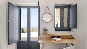 Una habitación con escritorio, puertas abiertas, un espejo redondo y vistas al exterior.