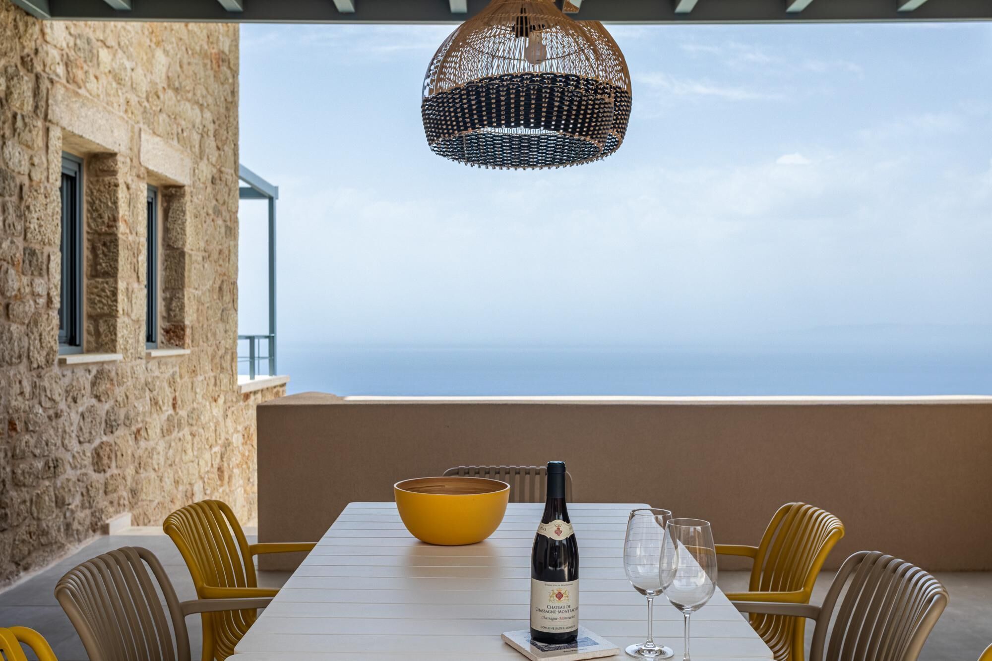 A table set with a bottle of wine, glasses, and a bowl, overlooking a scenic view.