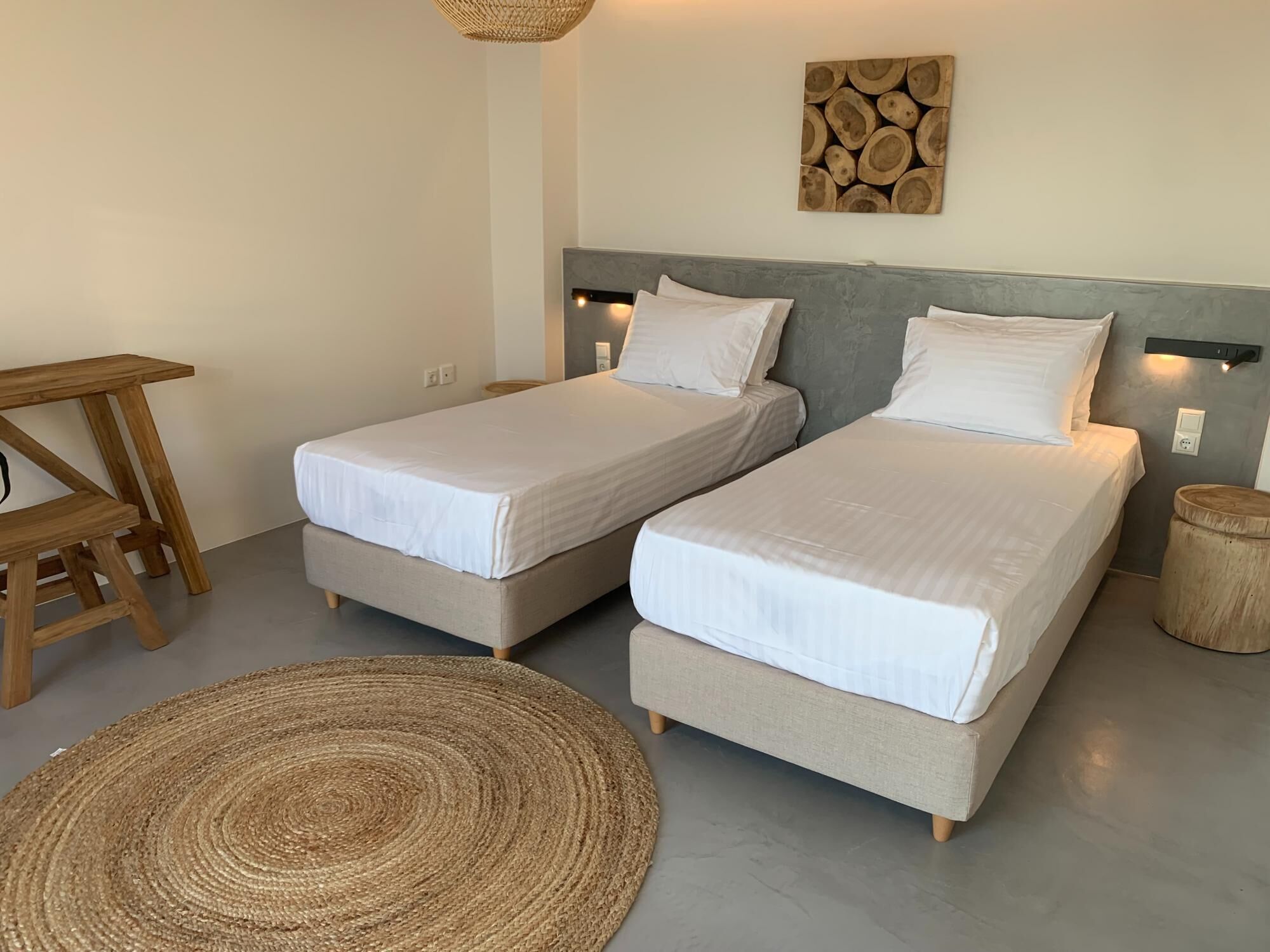 Een slaapkamer met twee eenpersoonsbedden, een houten nachtkastje, een geweven vloerkleed en een wandlamp.