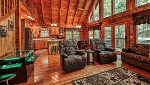 A spacious log cabin interior with a large dining area, two sofas, and a pool table.