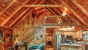 A spacious log cabin with a high ceiling, a central staircase, a kitchen area, and a cozy seating area.