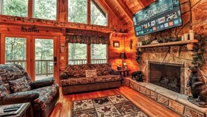 A cozy cabin interior with a fireplace, a television mounted on the wall, and a 'Welcome' sign above the door.
