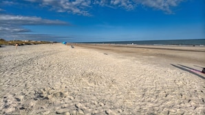 A sandy beach with footprints, a clear sky, and a distant shoreline. - (119) Heated Pool, Hot Tub, Walk to the Beach, Elevator, EV Charger (Hilton Head Island)