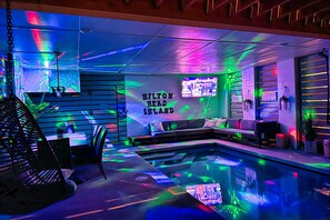 Een zwembadgedeelte met een neonverlicht plafond, een zitgedeelte met een bord 'Hilton Head Island' en een lounge met uitzicht op het zwembad.