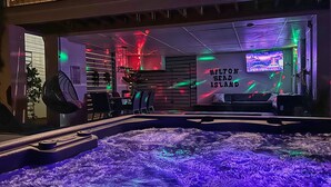 A room with a large, illuminated hot tub, a wall-mounted TV, and a sign reading "Hilton Head Island." - (119) Heated Pool, Hot Tub, Walk to the Beach, Elevator, EV Charger (Hilton Head Island)