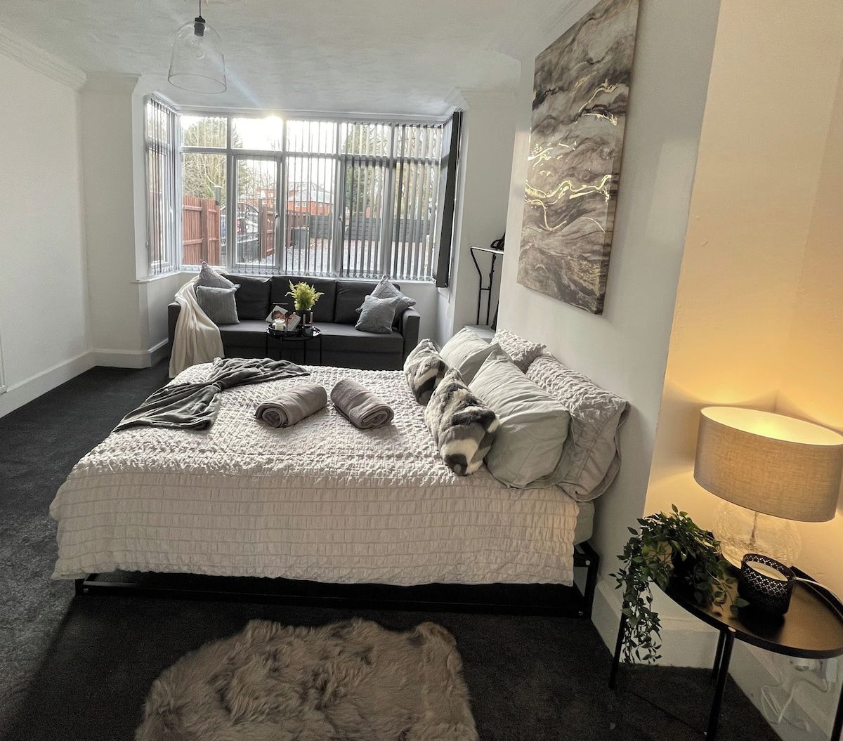 A bedroom with a large bed, a sofa, a lamp, and a view through a window.