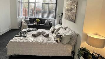 A bedroom with a large bed, a sofa, a lamp, and a view through a window.