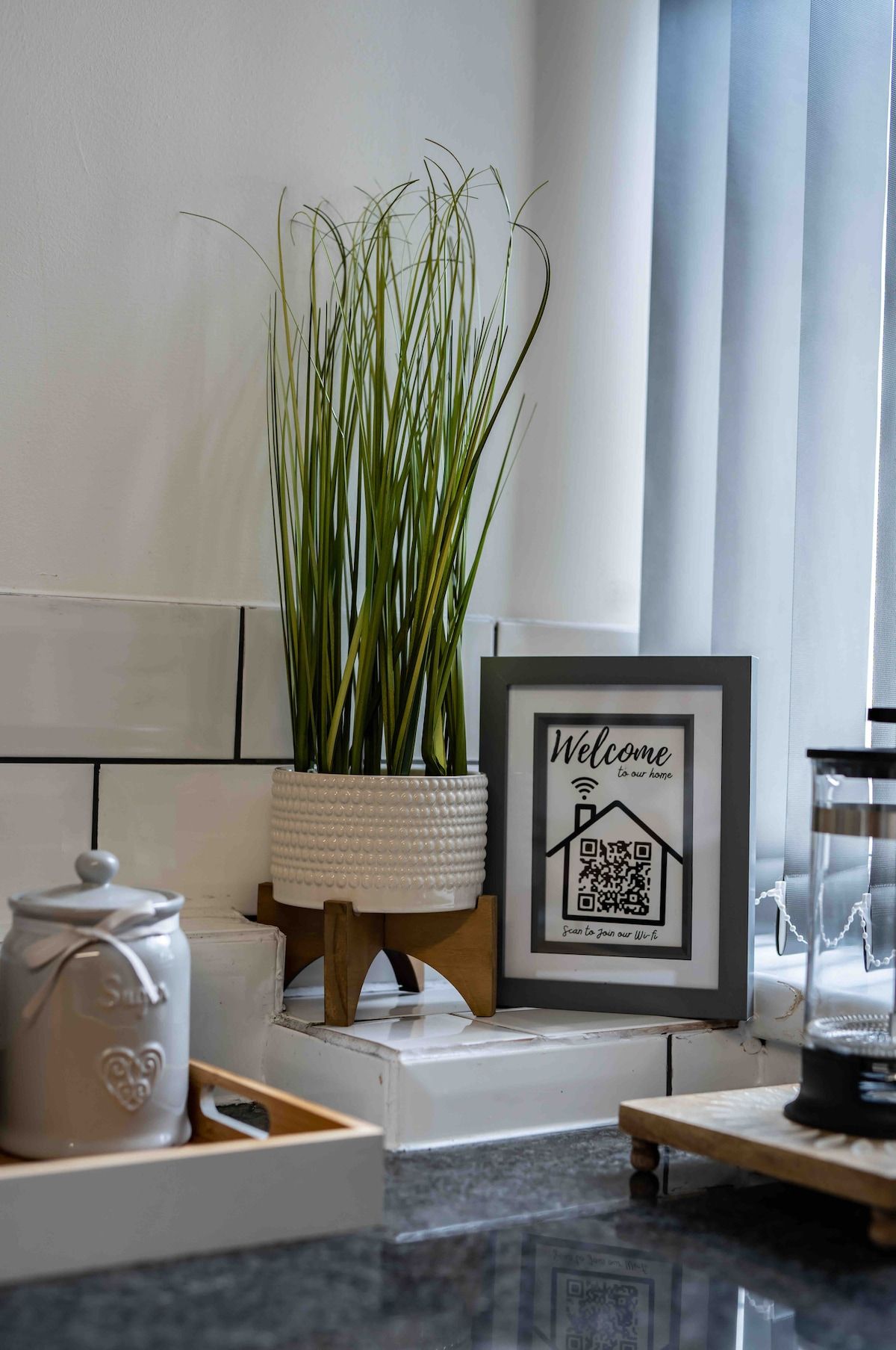 A potted plant, a framed welcome sign, a teapot, and a glass container on a countertop.