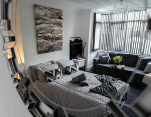 A modern bedroom with a bed, a seating area, and a large window.
