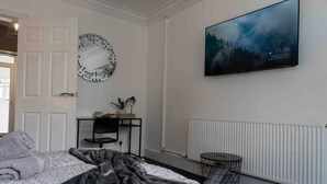 A bedroom with a bed, a round mirror, a desk with a chair, a round table, and a wall-mounted TV. - Casa Lobo's Beautiful Suites +free offroad parking (Wolverhampton)