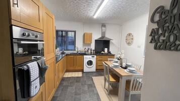 Una cucina compatta con mobili in legno, forno a incasso, lavatrice e zona pranzo con tavolo e sedie.