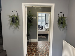 A hallway with a patterned floor leading to a bedroom with a bed and a window.