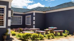 A house with a dark exterior, a tiled roof, and a garden with small plants and a few tables. - Ramatie Guest Palace (Kasane)