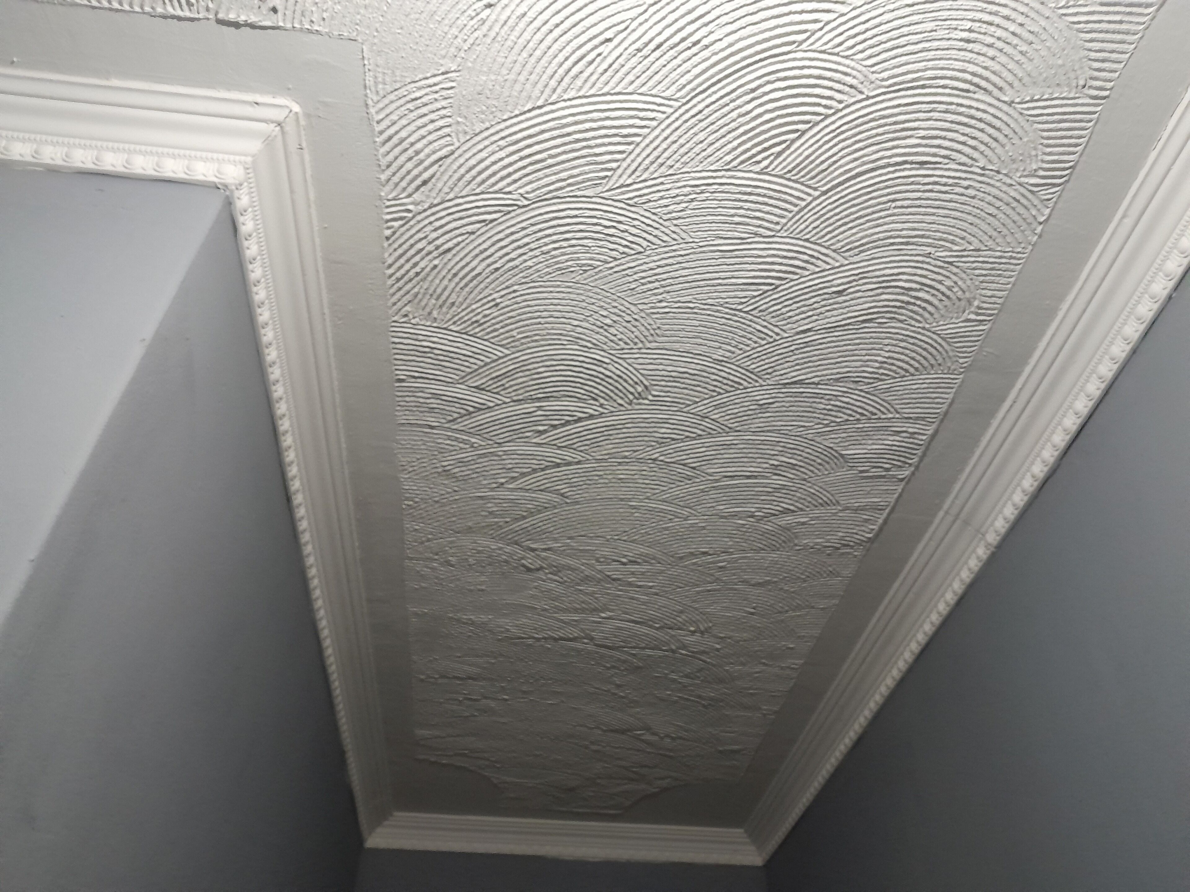 A corner of a room with a textured ceiling and a white trim.