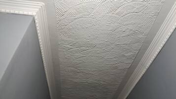 A corner of a room with a textured ceiling and a white trim.