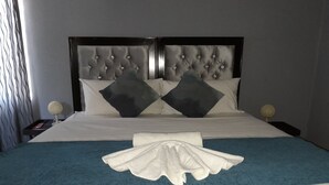 A neatly made bed with a tufted headboard, white linens, and a blue accent throw. - Ramatie Guest Palace (Kasane)