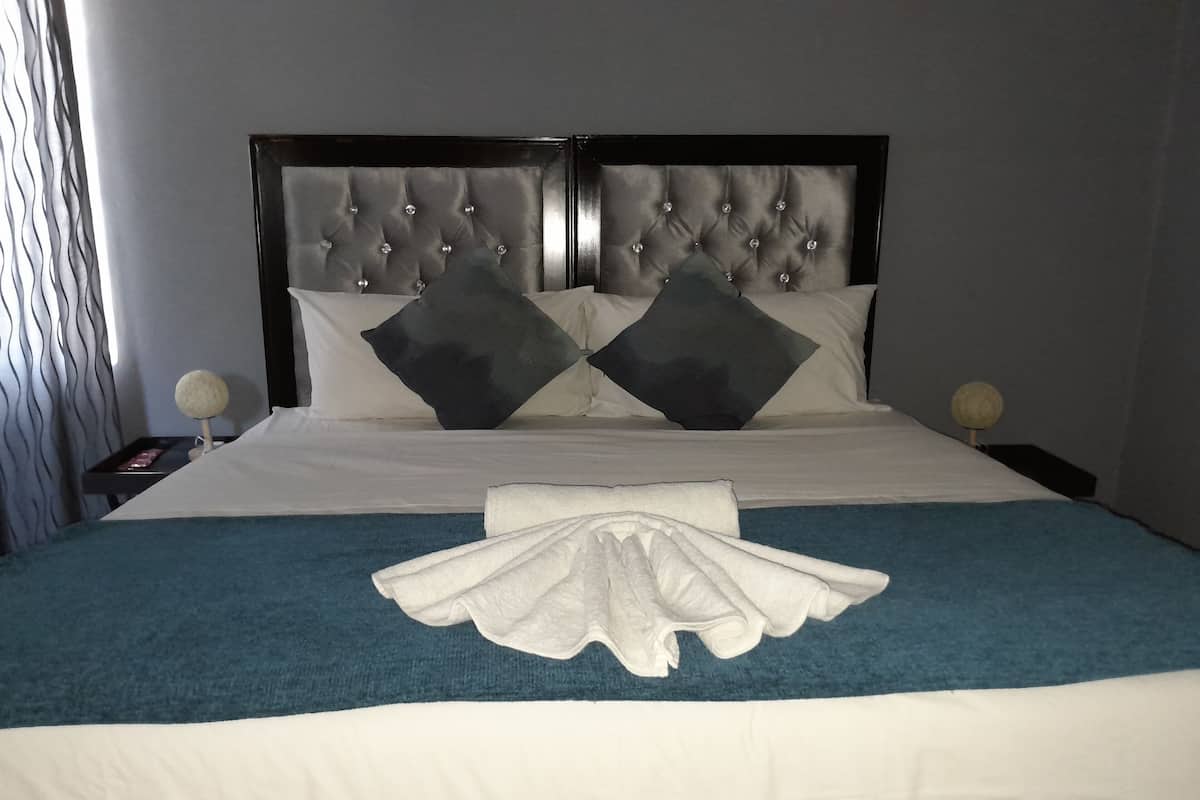 A neatly made bed with a tufted headboard, white linens, and a blue accent throw.