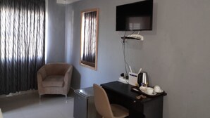 A hotel room with a sofa, a desk with a computer, a flat-screen TV, and a coffee maker. - Ramatie Guest Palace (Kasane)