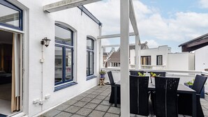Una terrazza sul tetto con tavolo e sedie, un edificio bianco con finestre a cornice blu e cielo sereno.