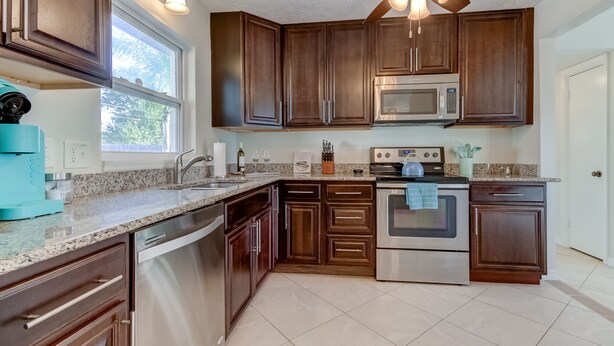 A modern kitchen with dark wood cabinets, stainless steel appliances, a granite countertop, and a ceiling fan. -  Few Mins to Madeira Beach, Comfortable, Dog Friendly (Seminole)