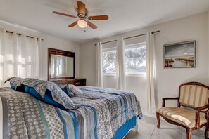 A bedroom with a bed, a chair, a ceiling fan, and a window with curtains.