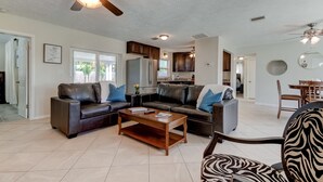 A spacious living room with a dark leather sofa, a wooden coffee table, and a ceiling fan. -  Few Mins to Madeira Beach, Comfortable, Dog Friendly (Seminole)