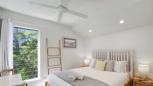A bedroom with a bed, bedside tables, a window with curtains, a ceiling fan, and a framed picture on the wall.