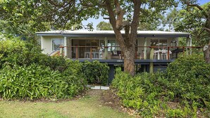 A two-story house with a balcony, surrounded by dense greenery.