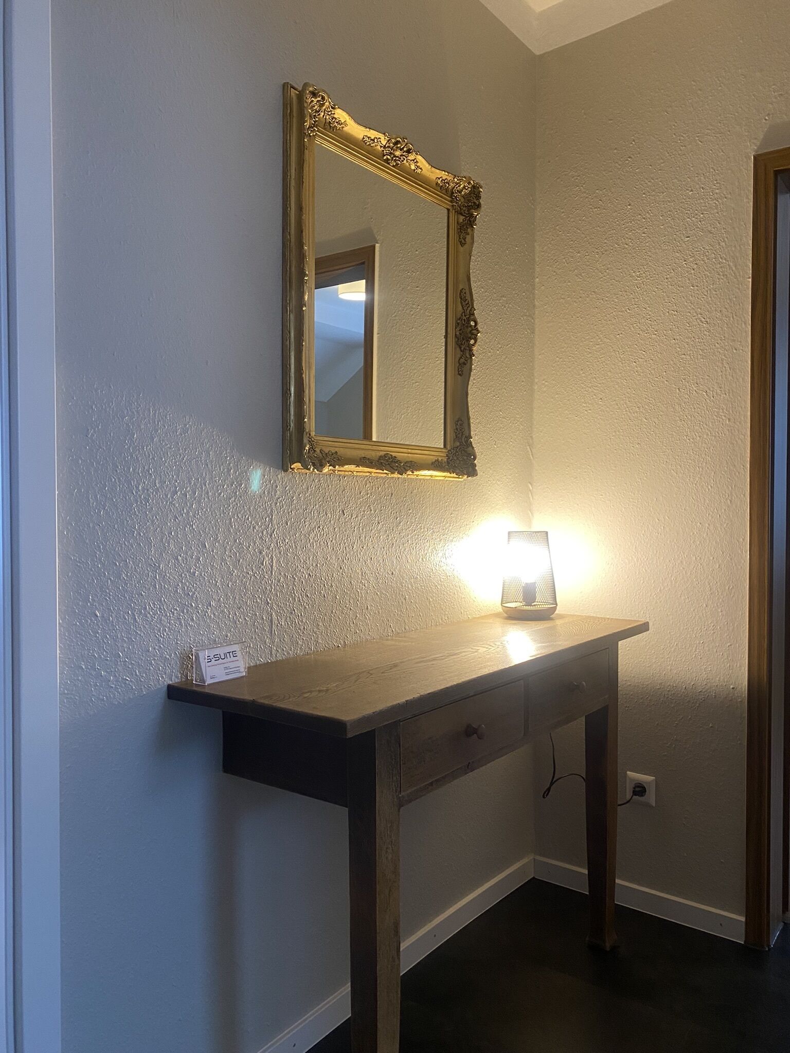 Una consola de madera con un espejo encima, una lámpara encendida sobre la mesa y un cartel que indica una suite.