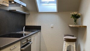A modern kitchen with a skylight, built-in oven, and a wooden stool.