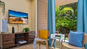 Un salon avec un téléviseur, des meubles en bois, une petite table et une vue sur la verdure à l’extérieur.