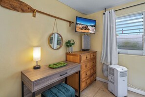 Une petite pièce comprenant un bureau en bois, un miroir, une télévision, un radiateur et une fenêtre avec des rideaux.