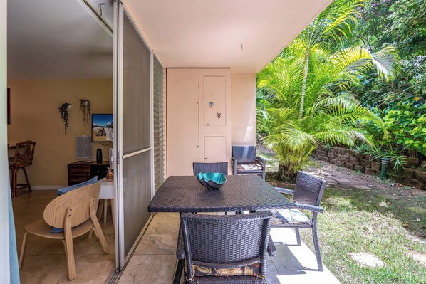Une terrasse avec une table et des chaises, une porte coulissante et une vue sur un jardin luxuriant.