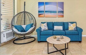 Un salon avec un canapé bleu, des coussins décoratifs, un fauteuil suspendu et une table ornée d’objets décoratifs.